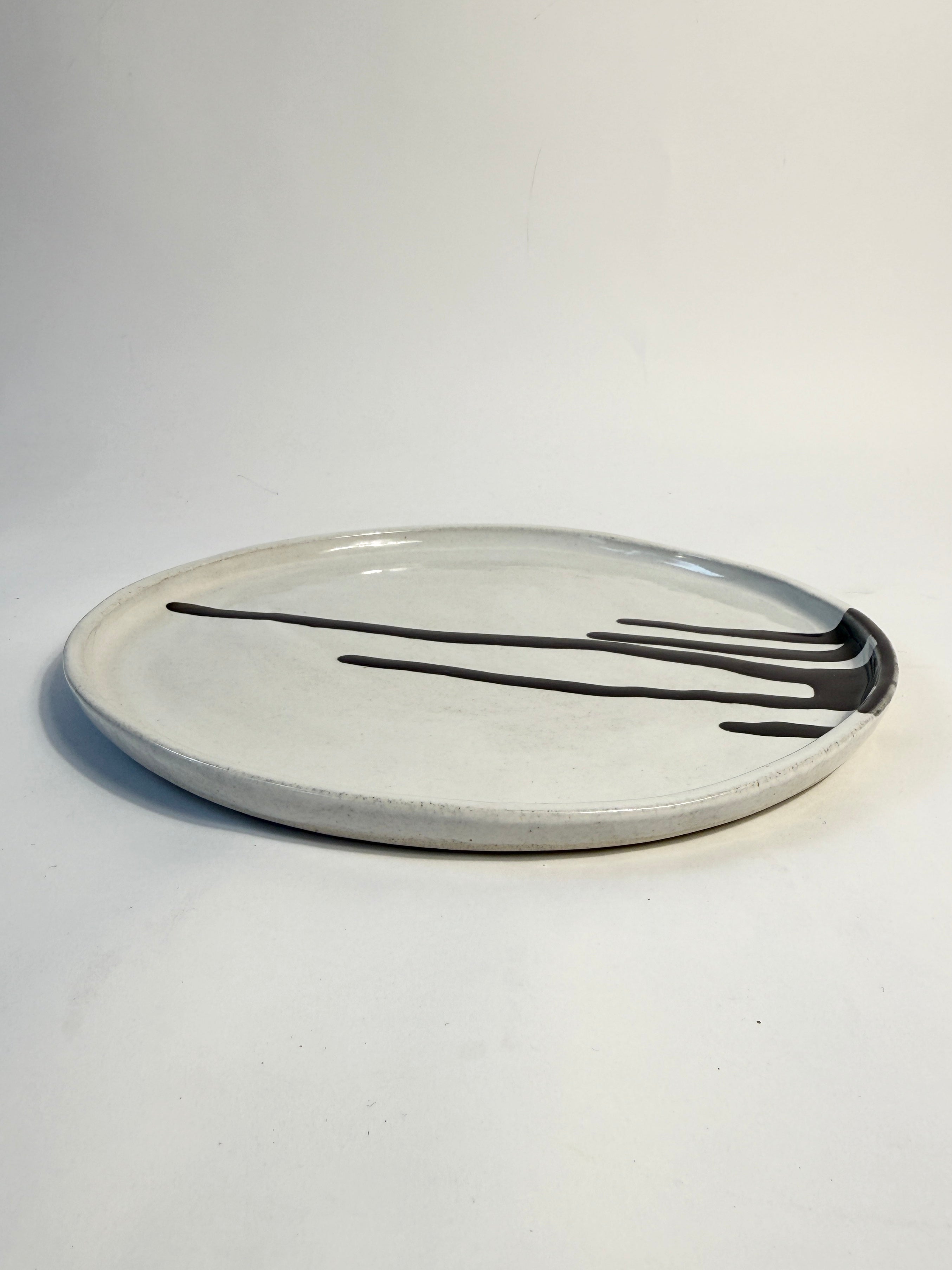 A round ceramic plate with a matte off-white glaze and abstract black glaze splatter design.  