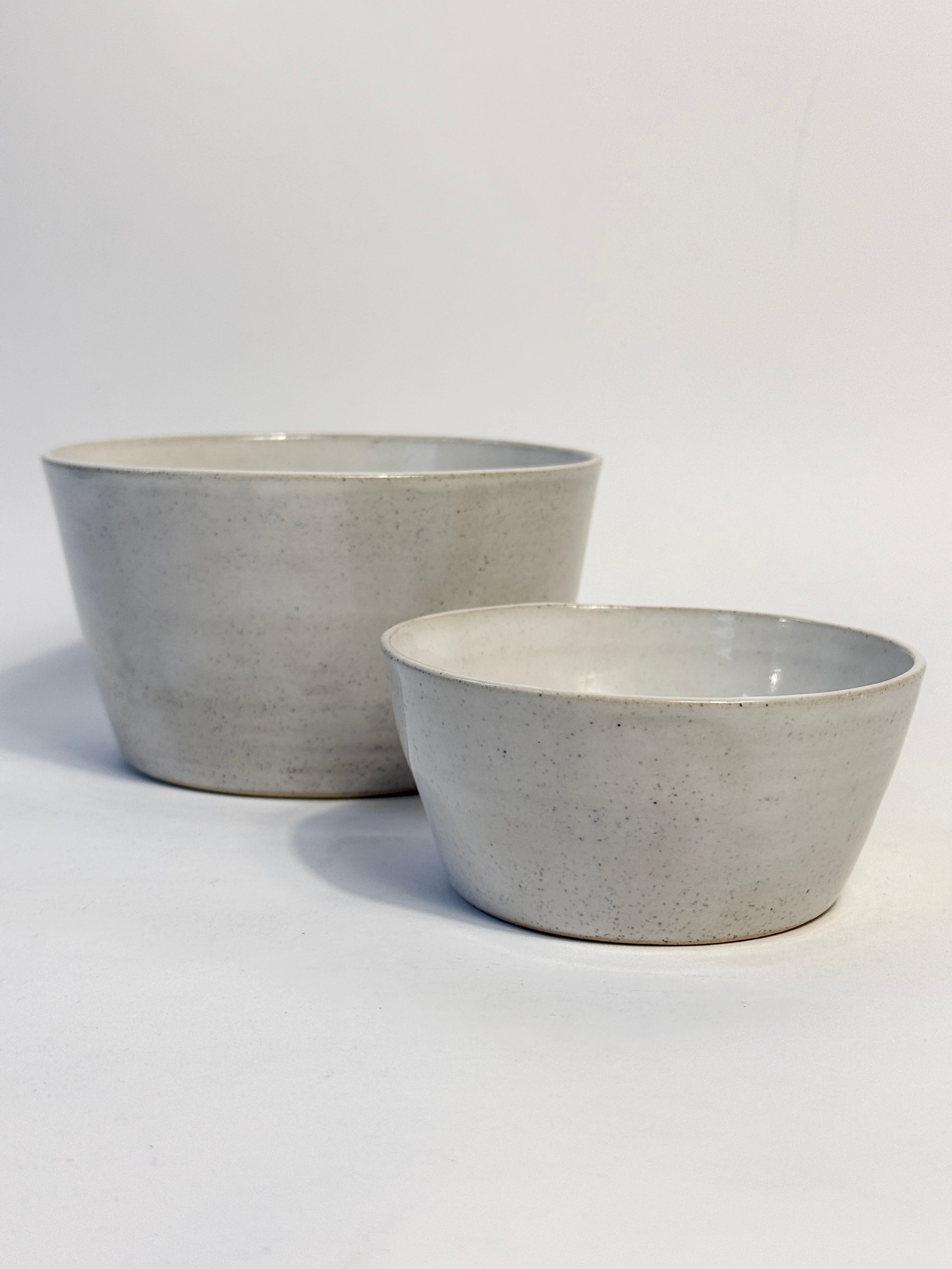 Two handmade ceramic bowls with a light speckled white glaze, one larger and one smaller. 