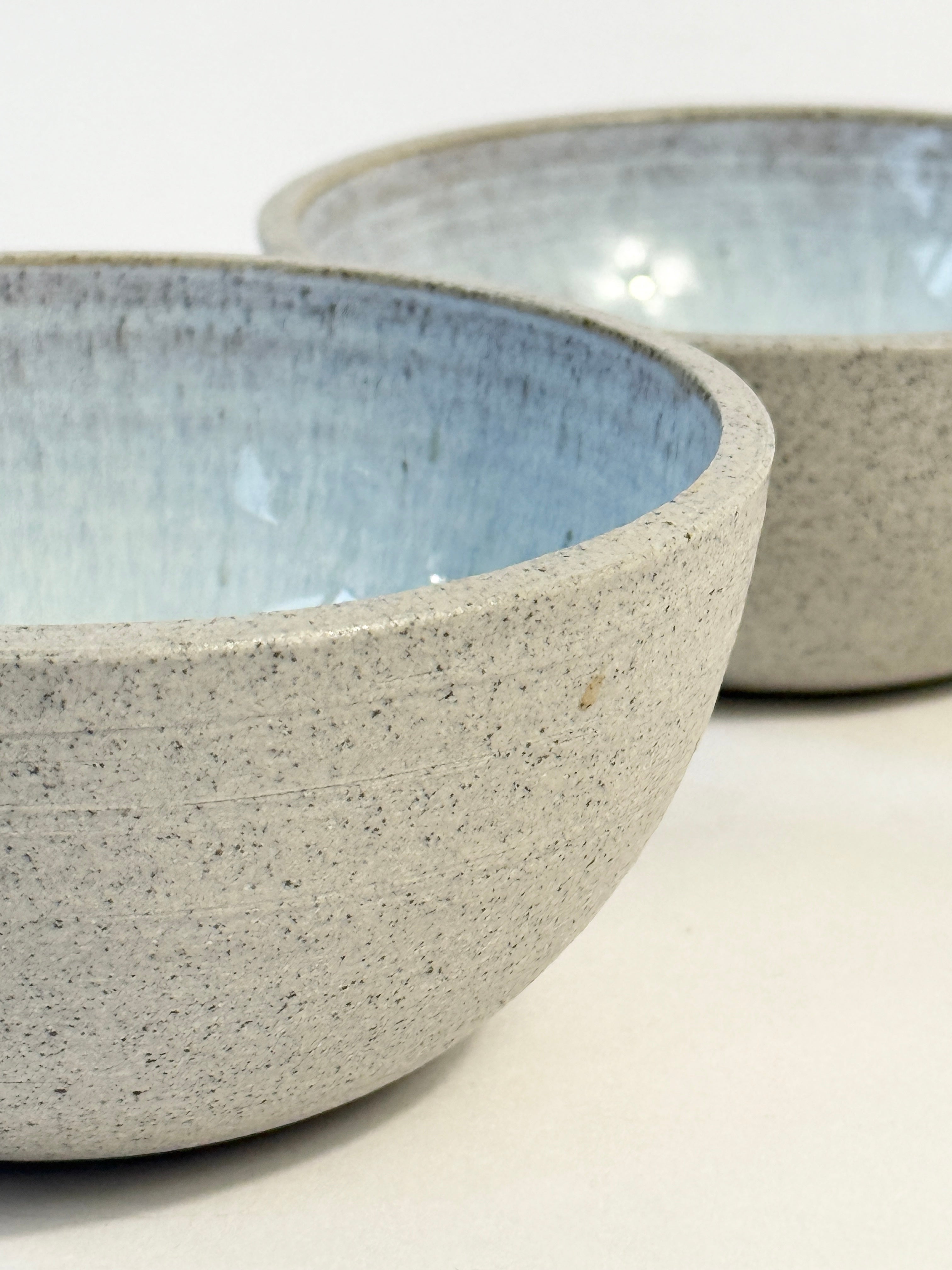 Two handmade ceramic bowls with speckled light gray exteriors and soft blue glazed interiors