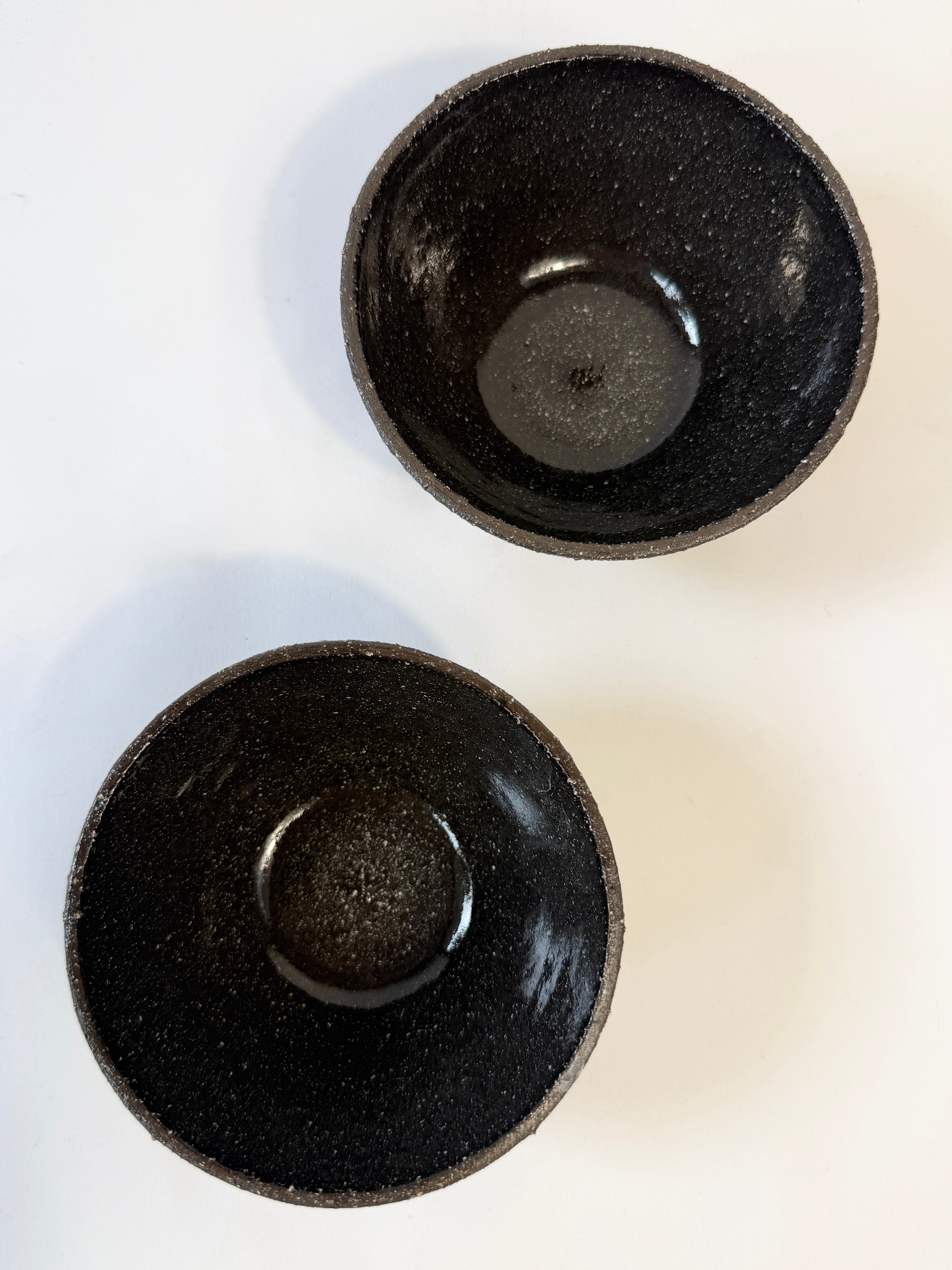 Two handmade dark speckled ceramic bowls shown from a top-down view.  Glazed interior and unglazed exterior.  Hand made in Adelaide