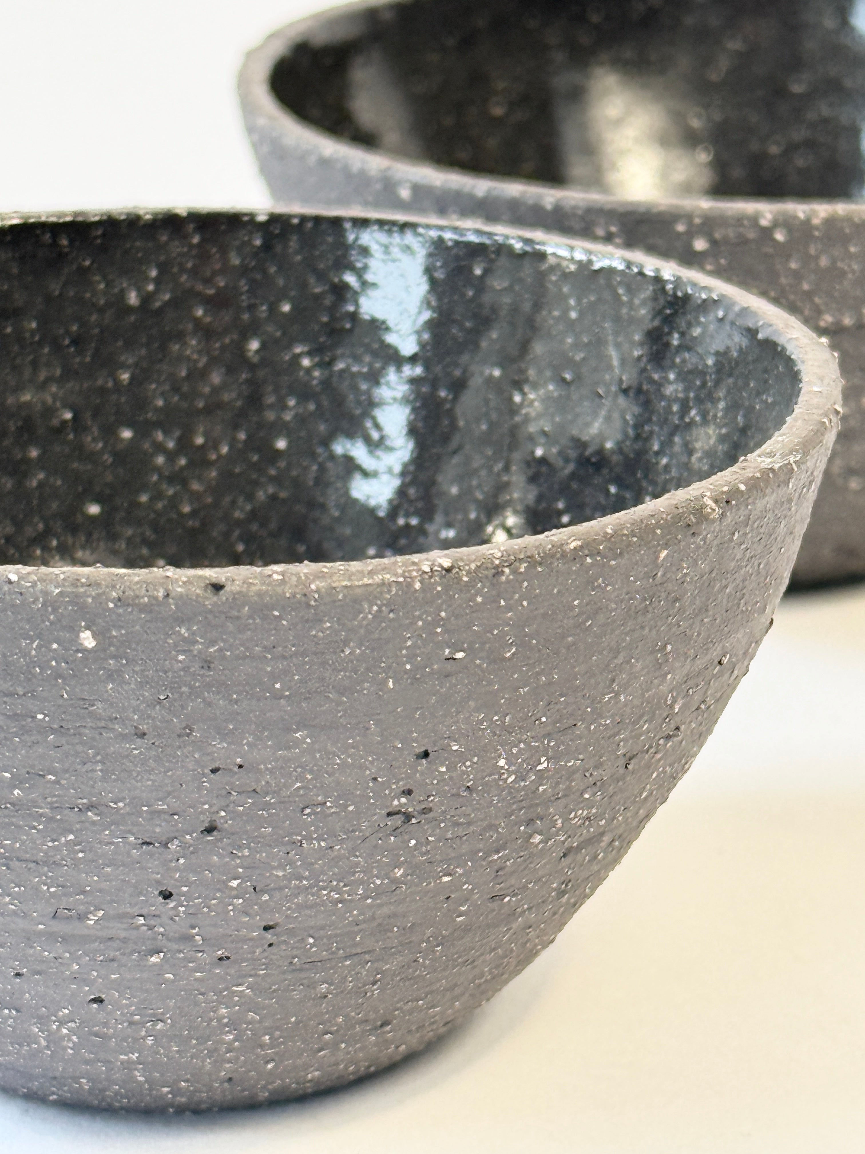 A close-up of a dark speckled hand made ceramic bowl with a glossy black interior.