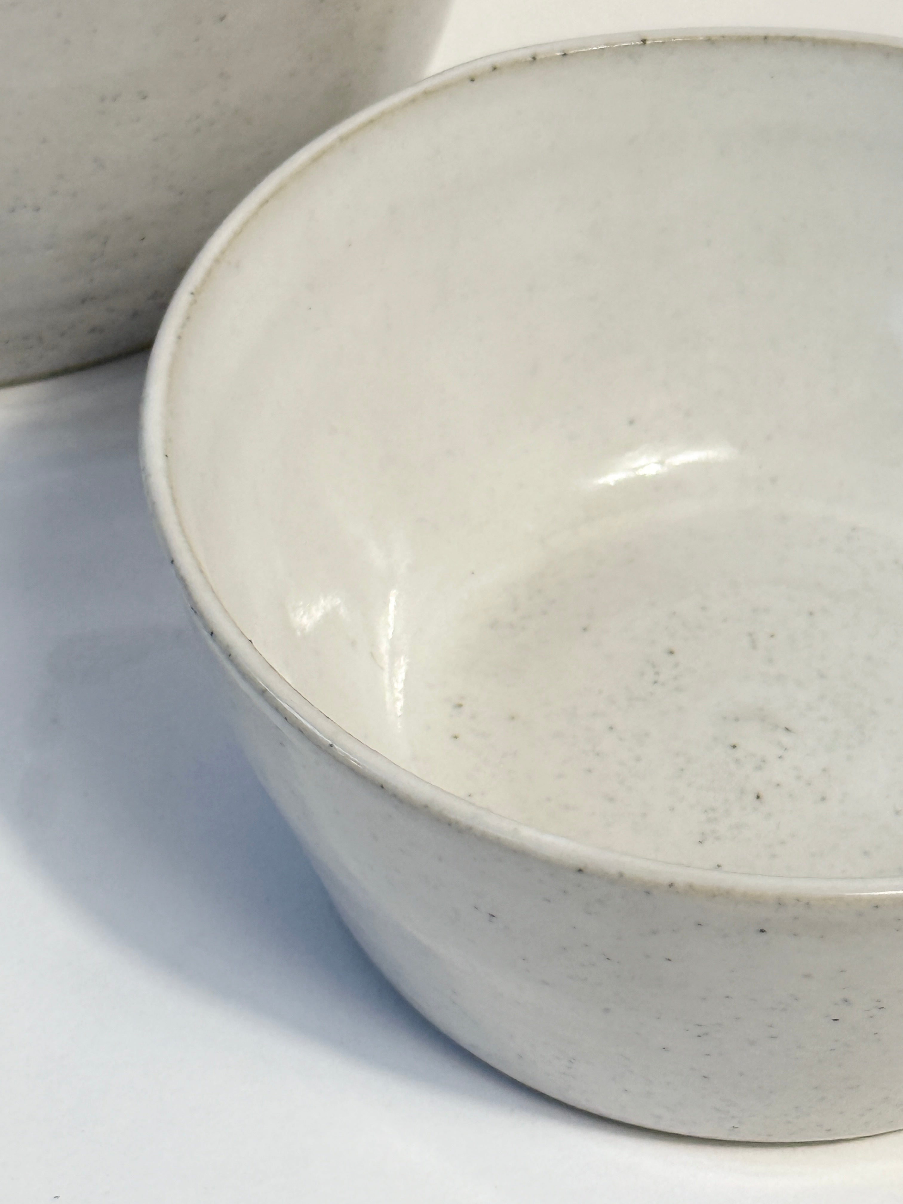 A close-up of a handmade ceramic bowl with a speckled white glaze, showing its smooth interior surface.