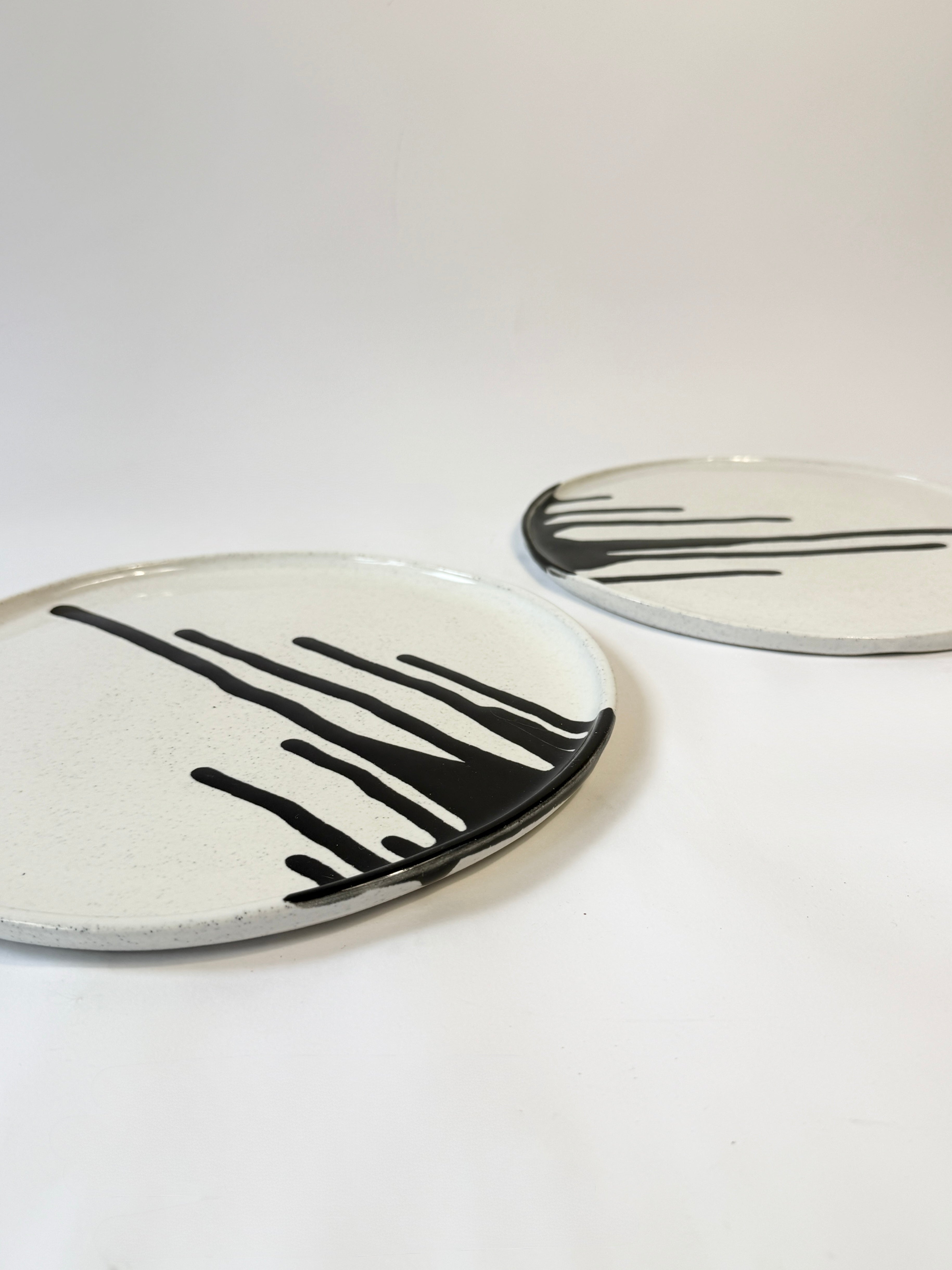 Two round ceramic platters with a white glaze and black abstract drip lines and created with speckled white clay. 