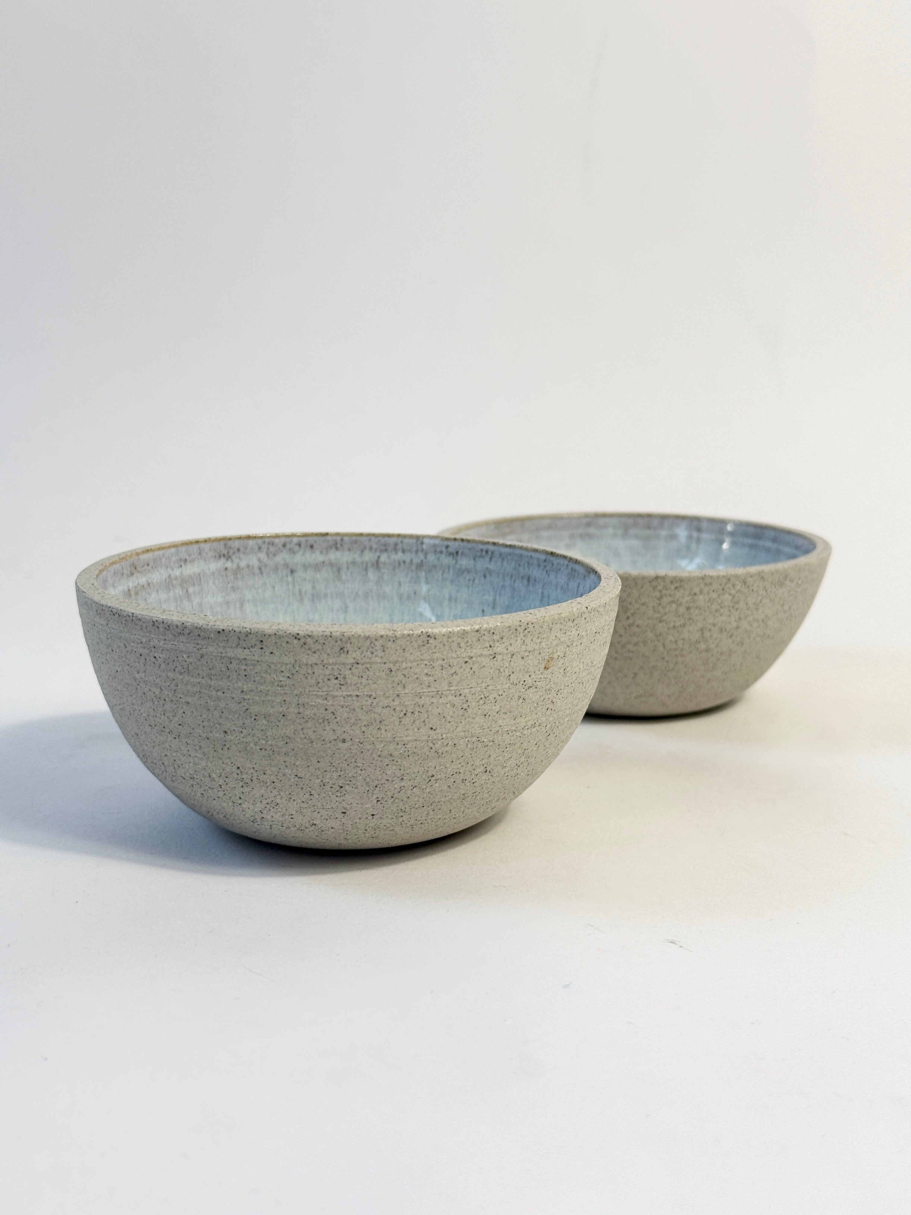 Two handmade ceramic bowls with a speckled light gray exterior and a glazed light blue interior