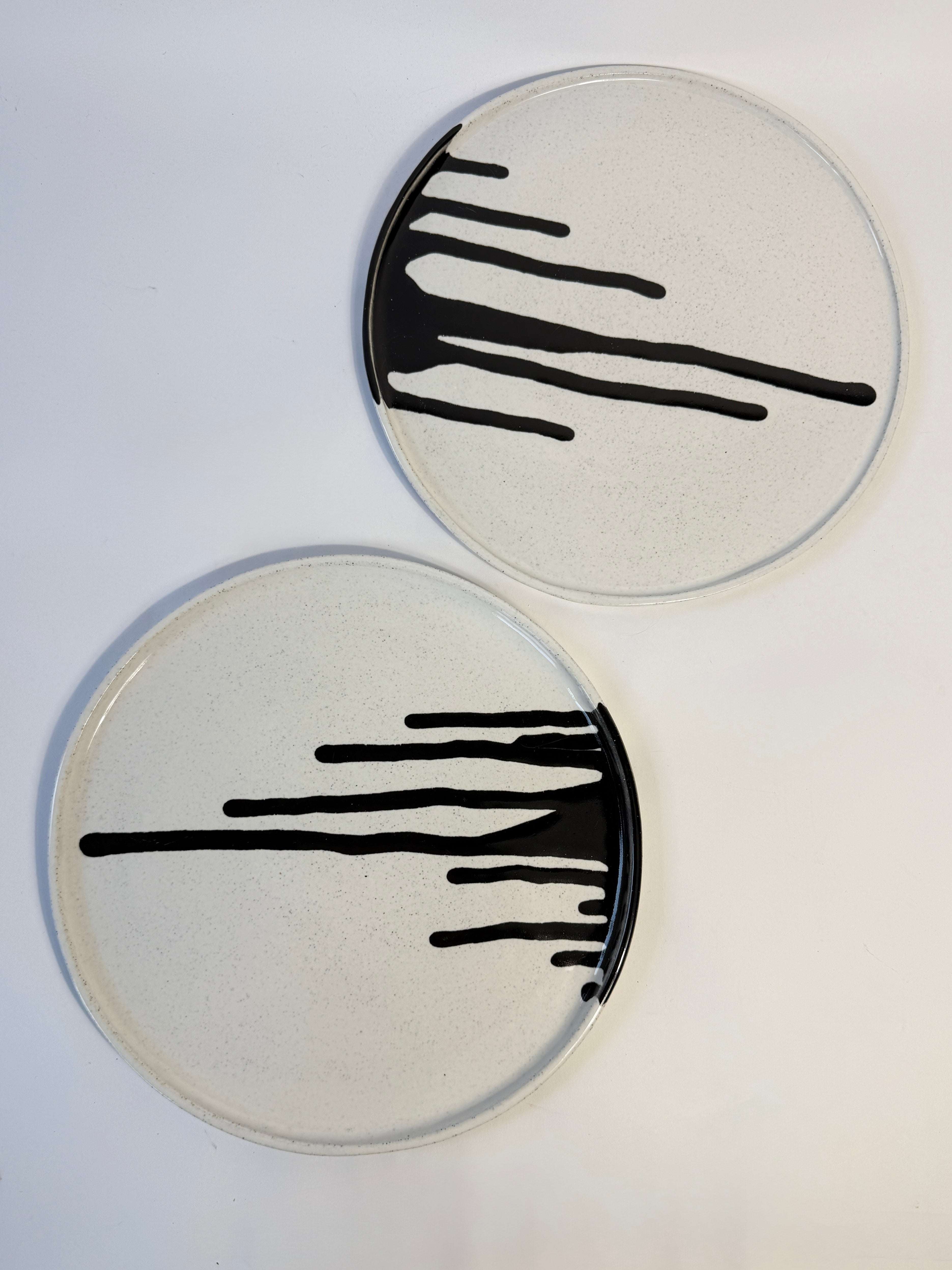 Two round ceramic platters / plates created from speckled clay with off-white glaze and black drip-style black glaze decoration