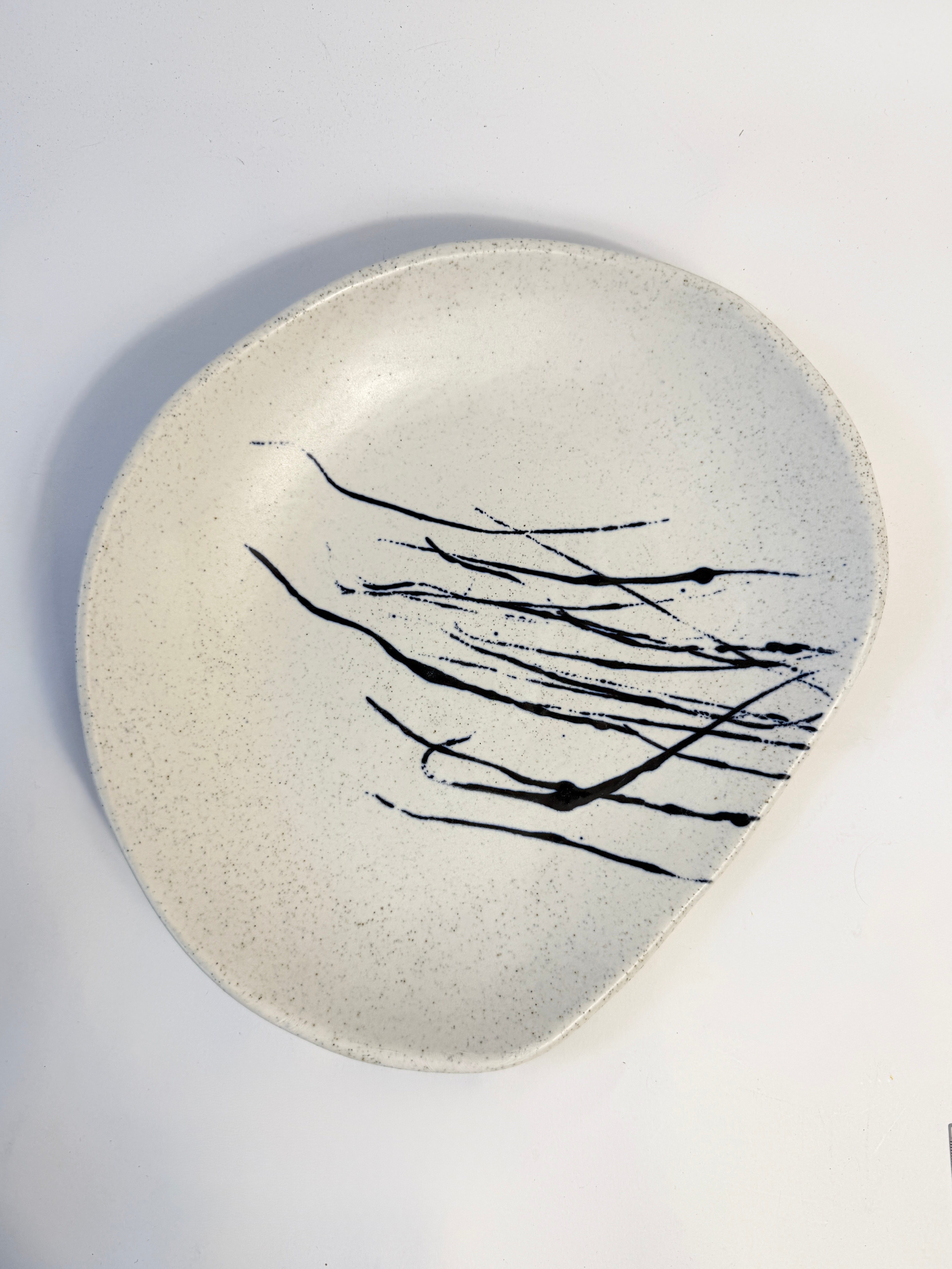 An organic shaped speckled ceramic plate in a warm off-white glaze, decorated with black glaze splatters. Hand made in Adelaide